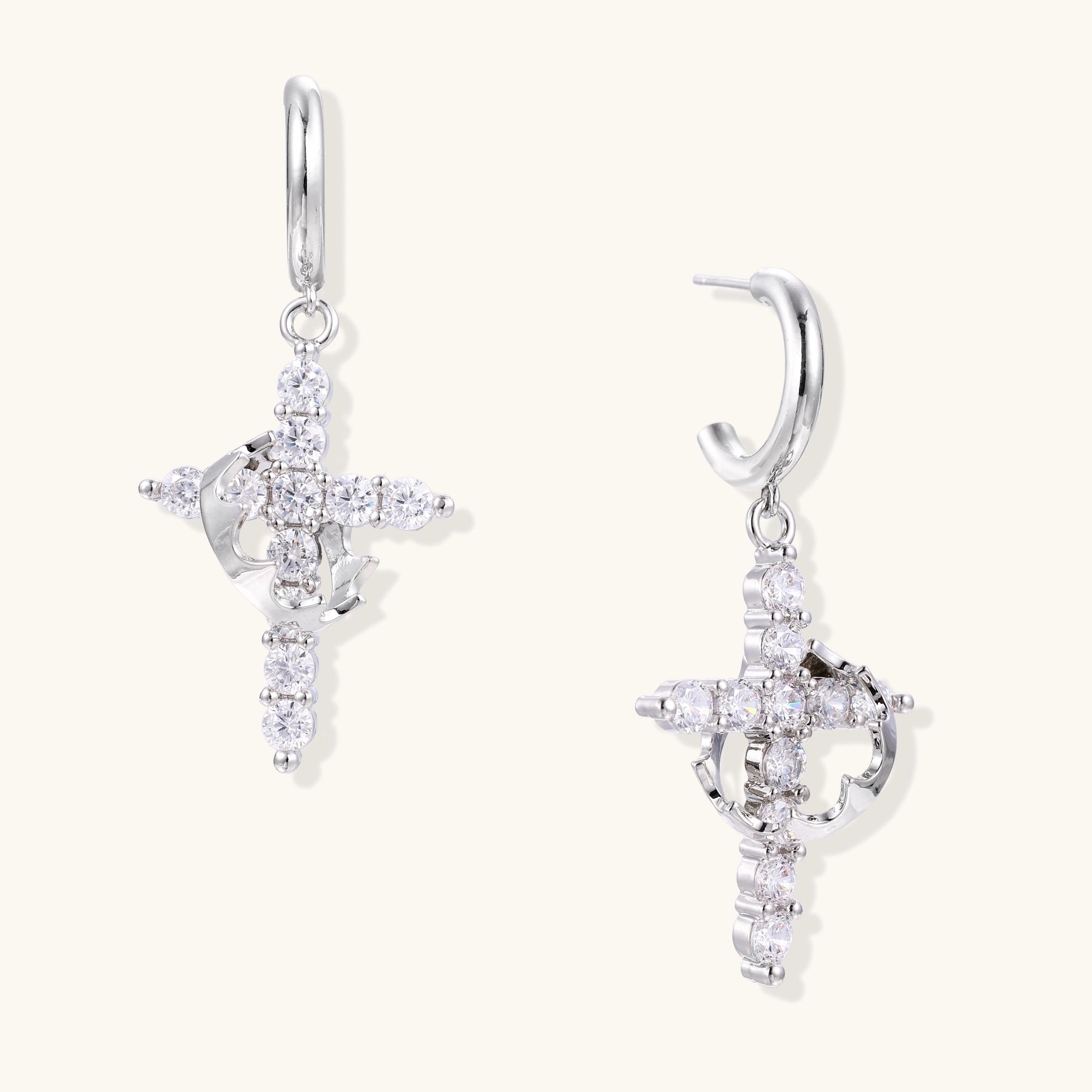 White gold-plated hoop earrings with sparkling zirconia cross charms dangling against cream background