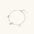 Delicate rhodium-plated silver chain bracelet with butterfly charm and two freshwater pearls on cream background