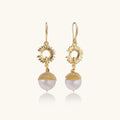 Gold sunburst charm earrings with baroque pearl drops on French hooks against cream background