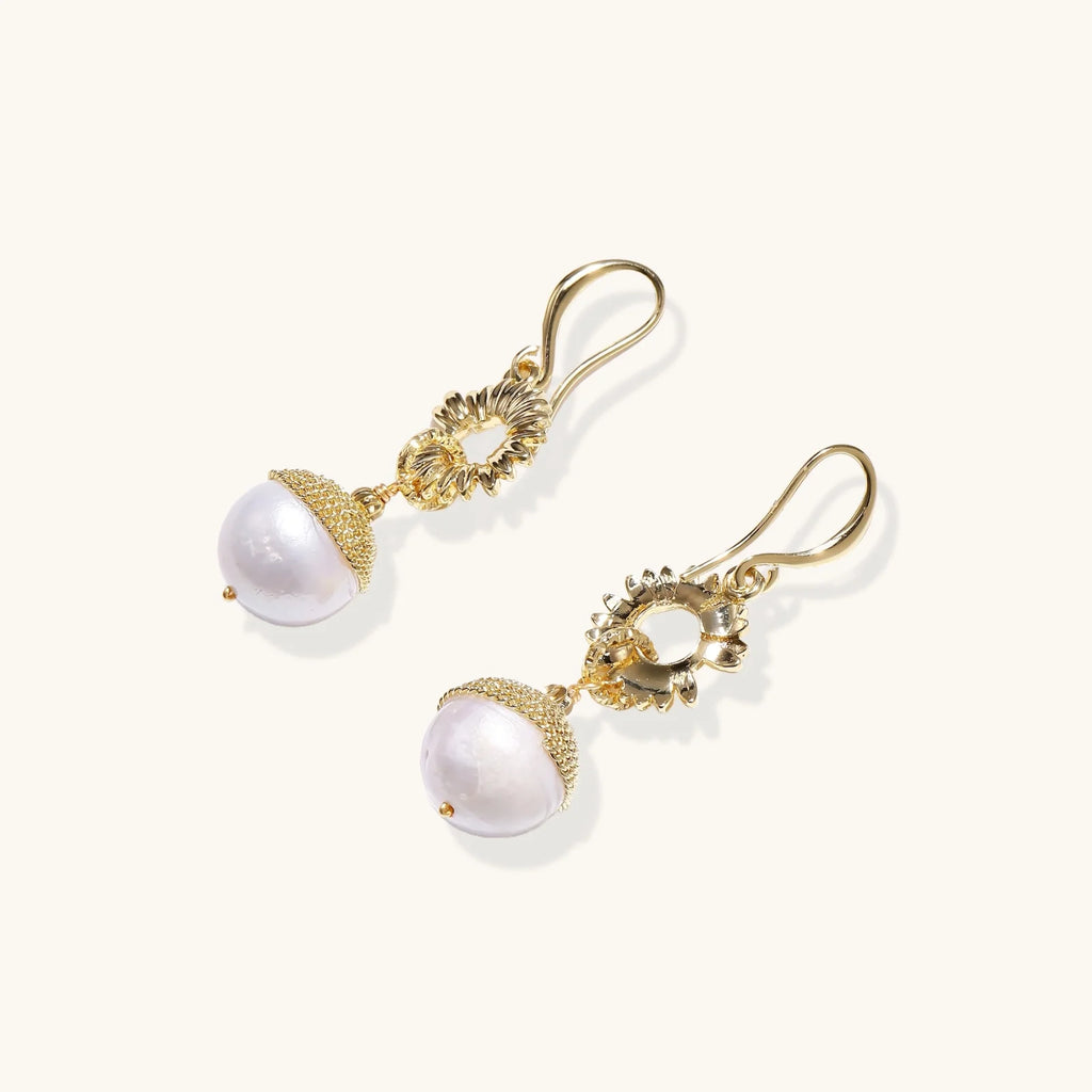 Gold sunburst charm earrings with baroque pearl drops on French hooks against cream background