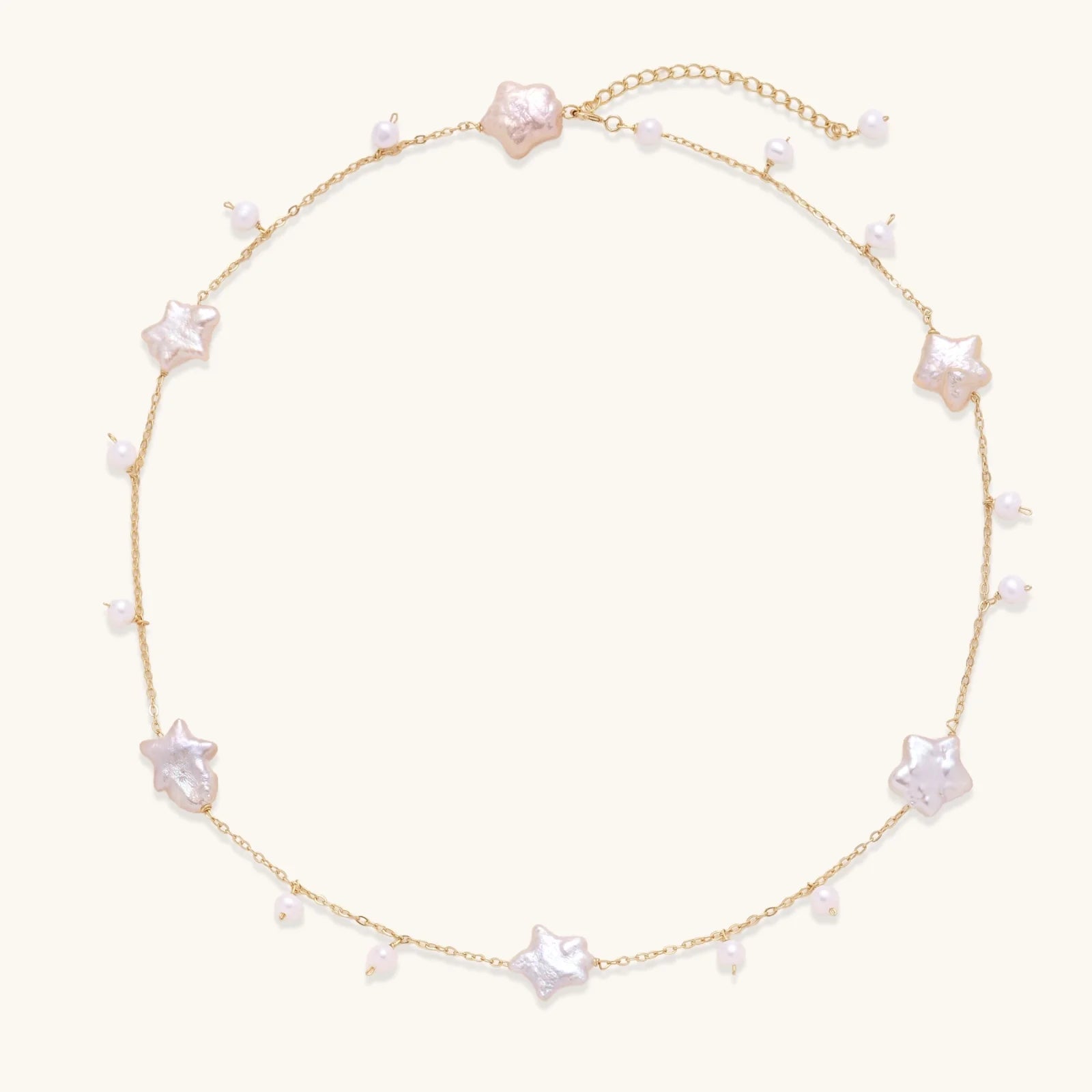 Gold vermeil chain with iridescent star-shaped baroque pearls and small round freshwater pearl drops on cream background.