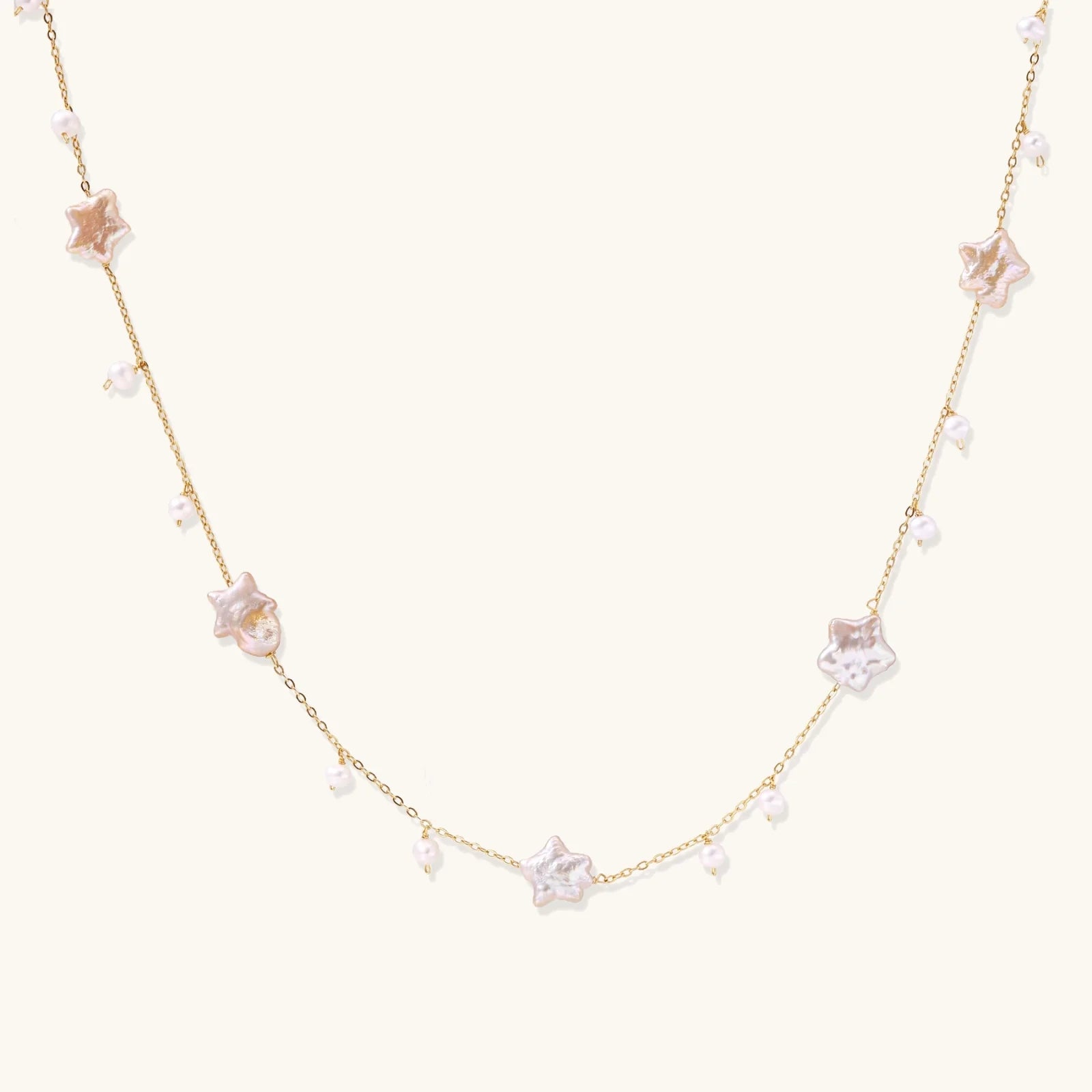 Gold vermeil chain with iridescent star-shaped baroque pearls and small round freshwater pearl drops on cream background.