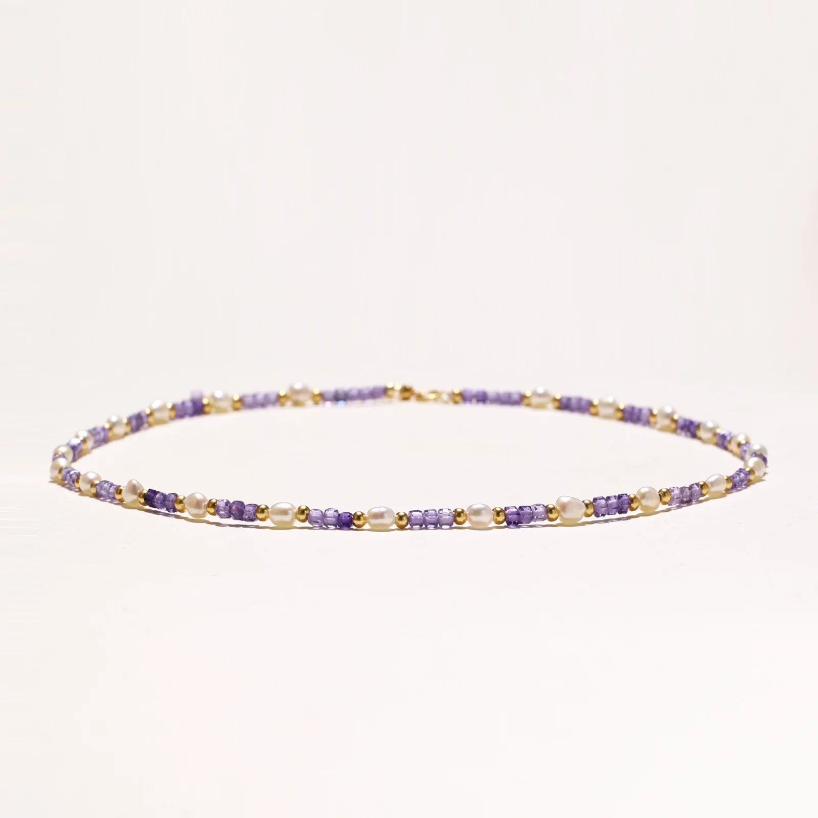Delicate 18K gold vermeil necklace with alternating lavender zirconia beads and white freshwater pearls on cream background