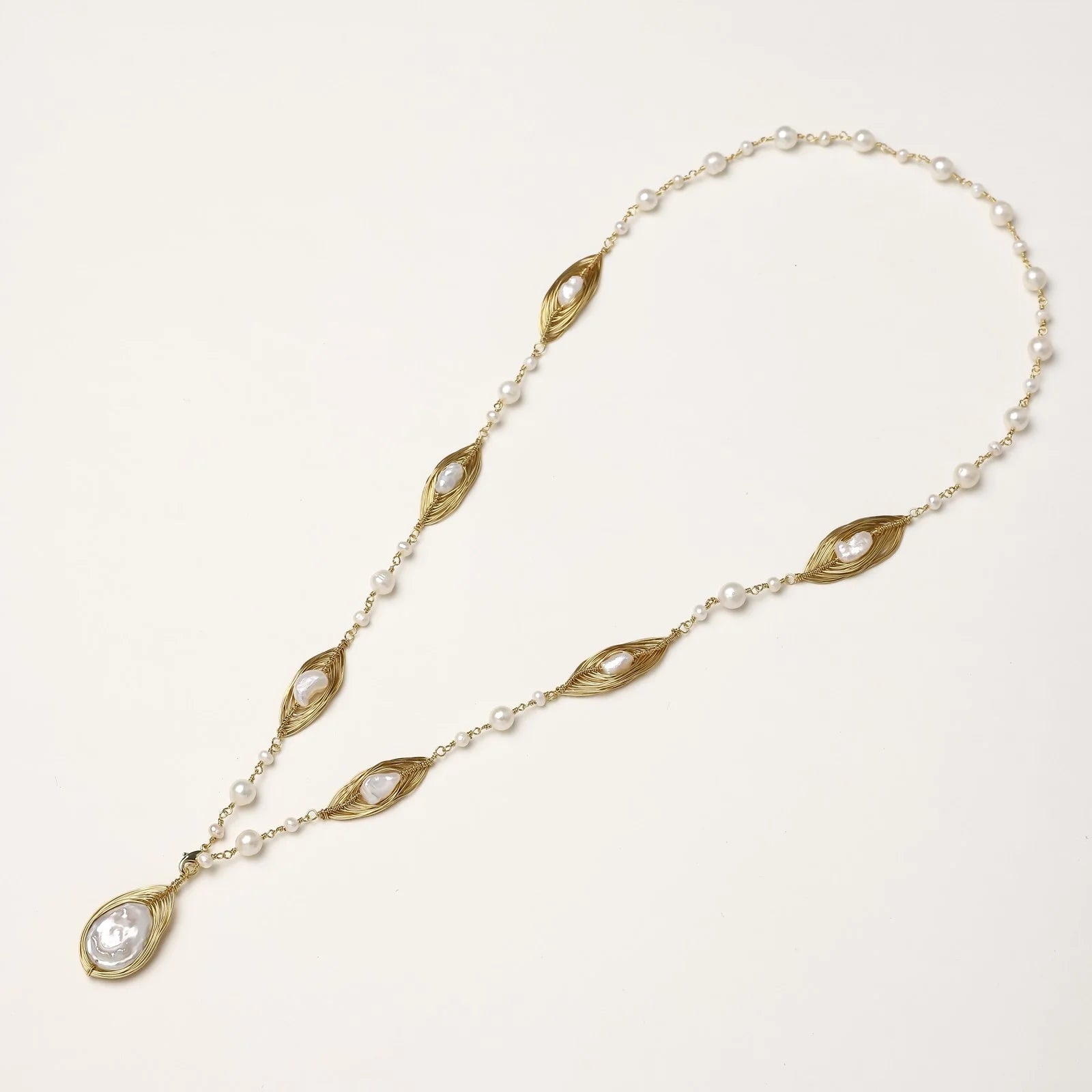 14K gold-plated necklace with eye-shaped stations and baroque pearl pendant on cream background