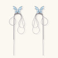 Long silver-tone earrings with powder blue enamel butterfly studs and flowing chain tassels on cream background