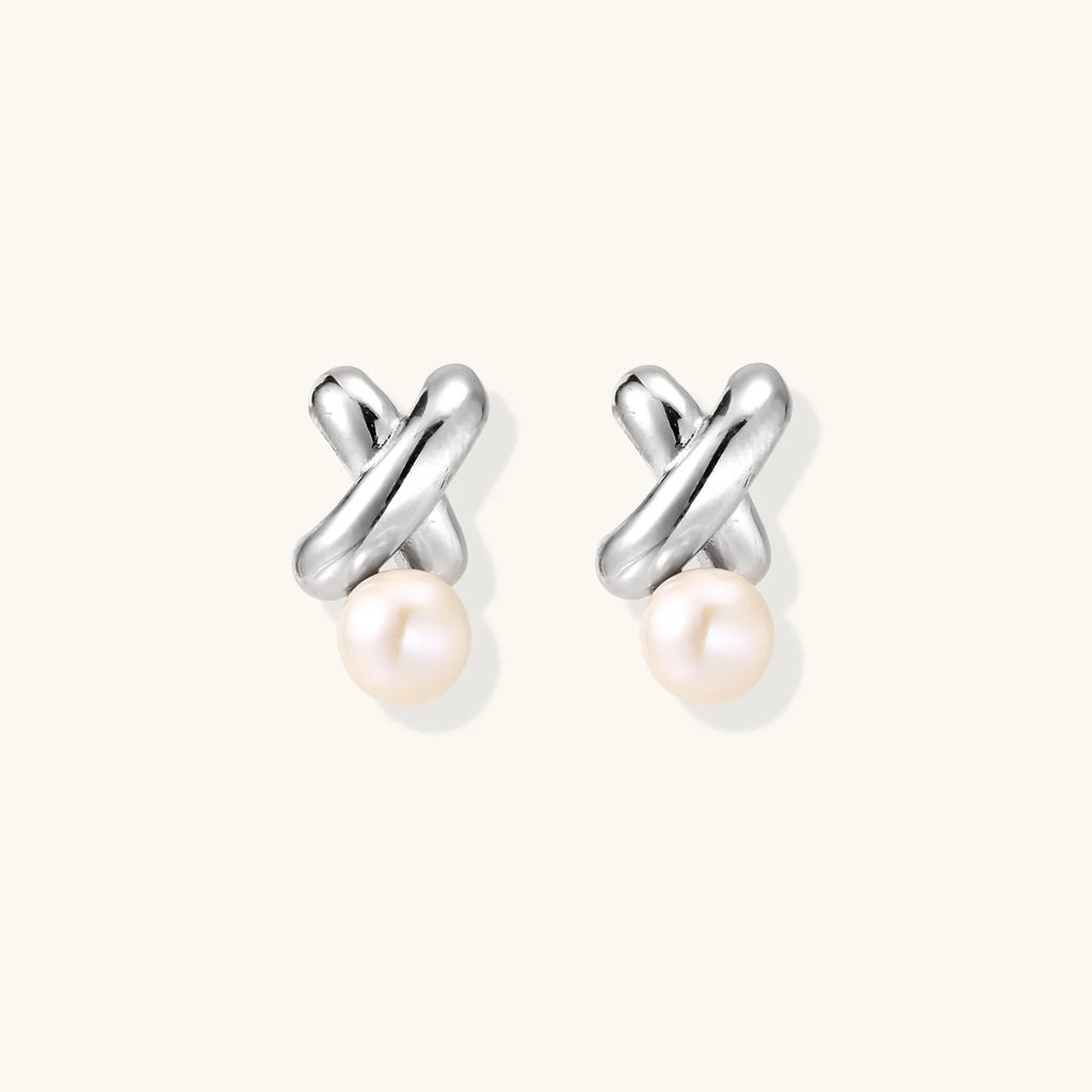 Rhodium-plated silver earrings with twisted X design and freshwater pearl drops on beige background
