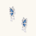 Silver butterfly earrings with blue denim fabric wings and dangling teardrop crystals on cream background