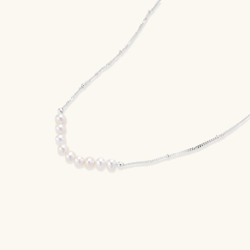 Delicate sterling silver chain necklace with small freshwater pearls arranged in a curved smile arc on cream background.
