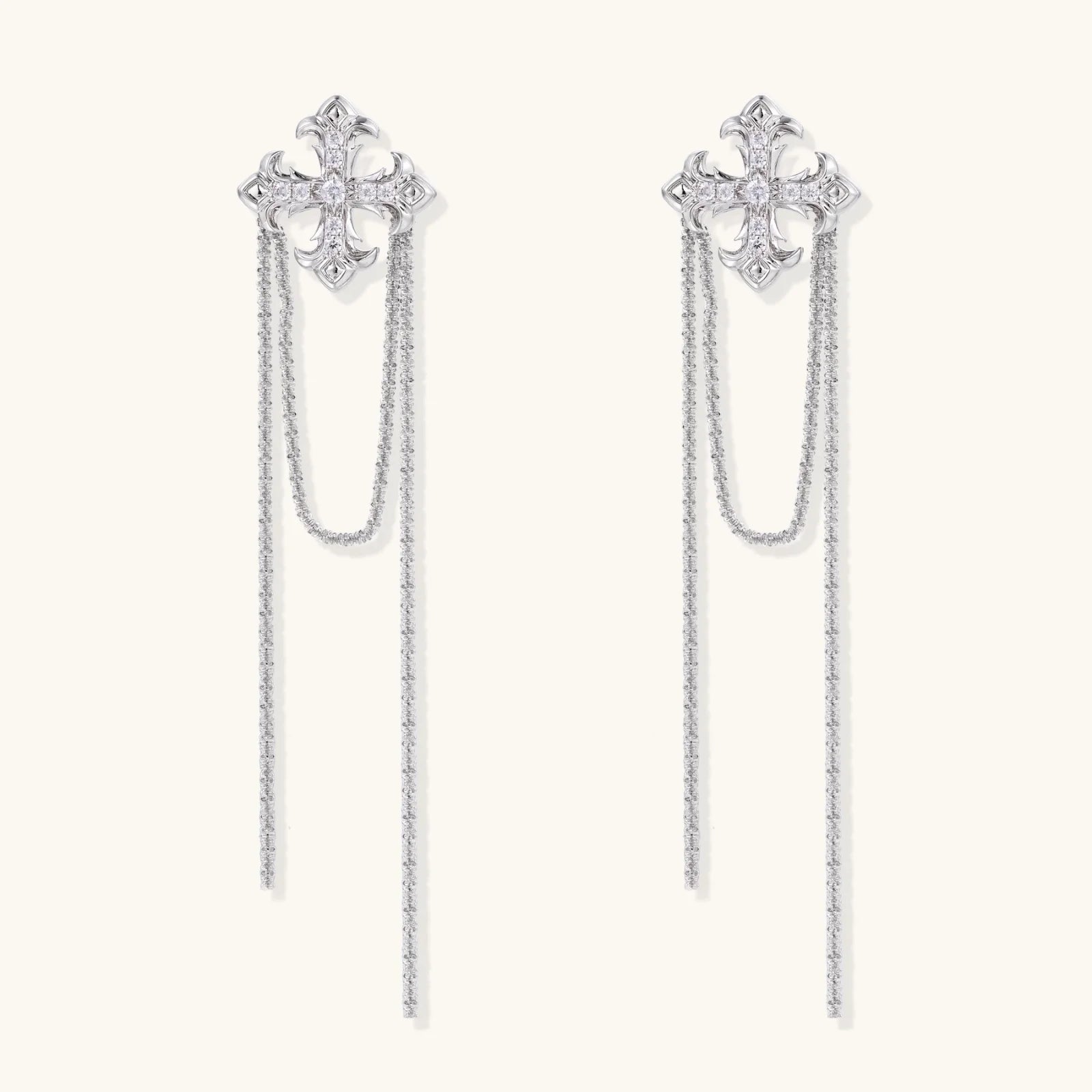 White gold plated baroque cross stud earrings with long cascading zirconia chains on cream background
