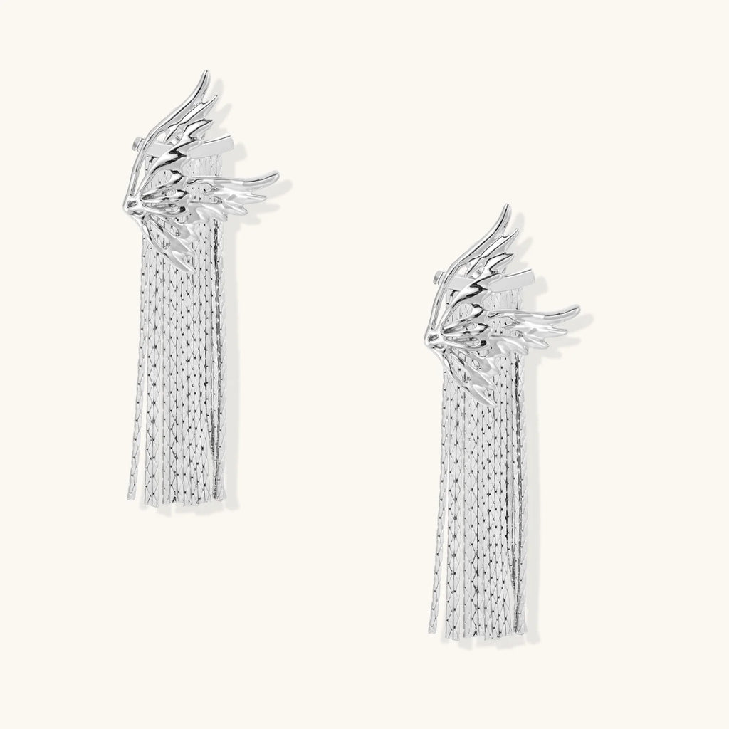 Sculptural white gold plated wing earrings with long chain tassel fringe on cream background