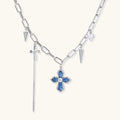 White gold plated chain necklace with blue textured cross pendant, spike charms, and mini cross detail on beige background