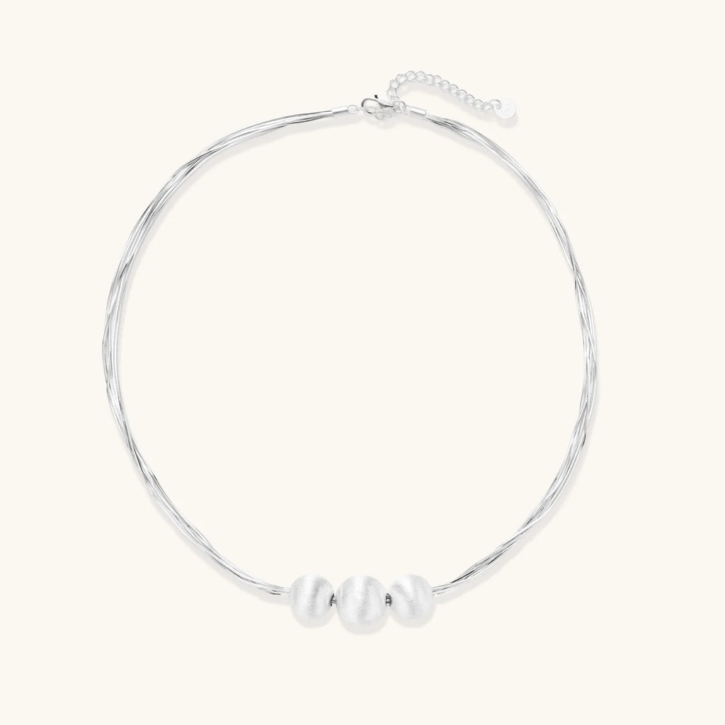 Sterling silver multi-strand necklace with three brushed round beads on cream background