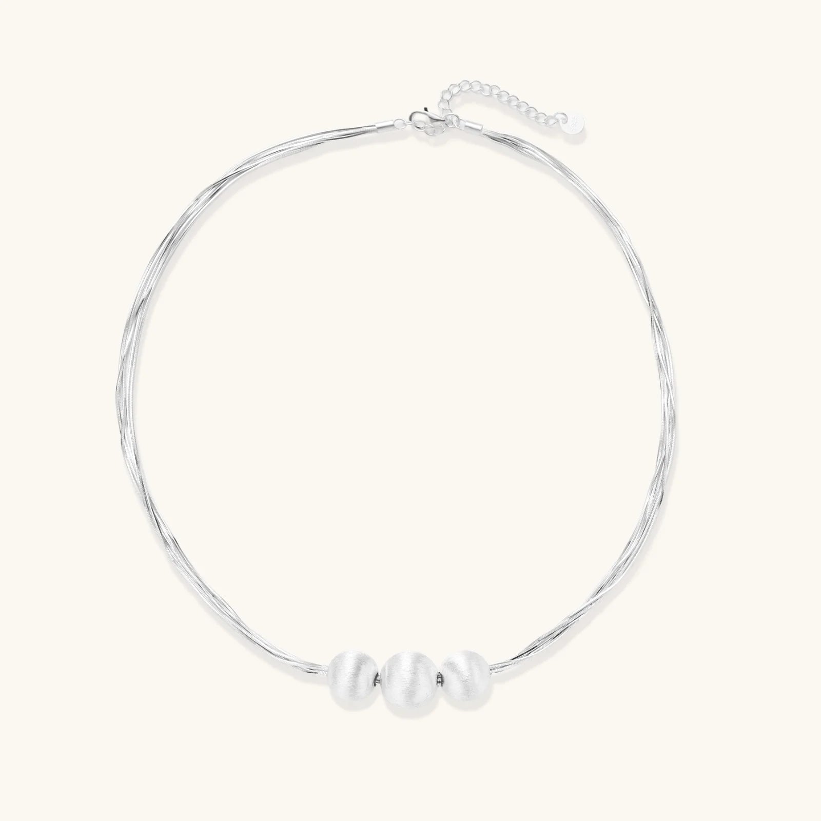 Sterling silver multi-strand necklace with three brushed round beads on cream background