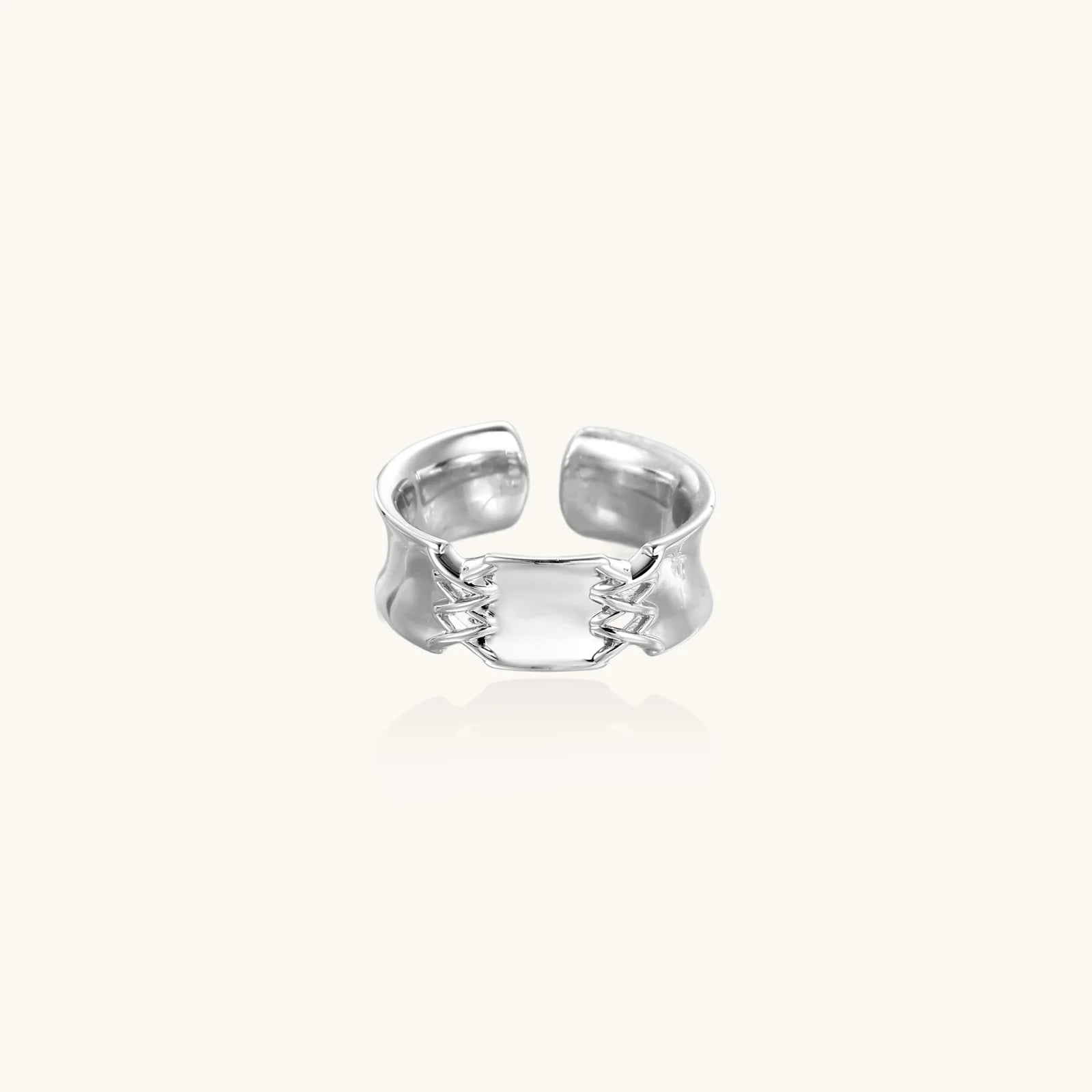 Adjustable silver-toned ring with sculptural stitch design across polished white gold-plated brass band