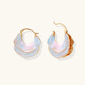 Shell-shaped hoop earrings with iridescent blue-pink enamel and gold trim on cream background