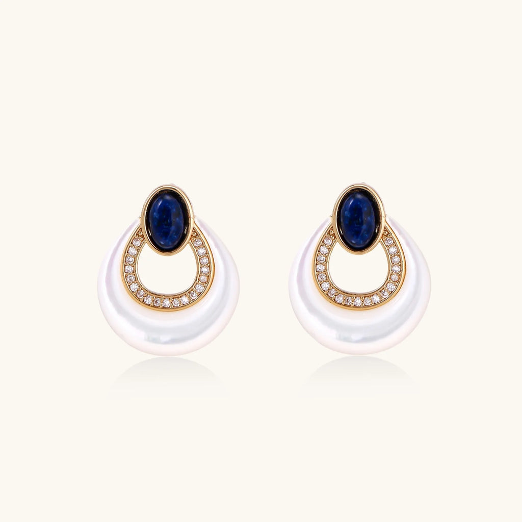 Gold drop earrings with oval lapis lazuli, crystal-paved frame, and iridescent mother-of-pearl teardrop on cream background