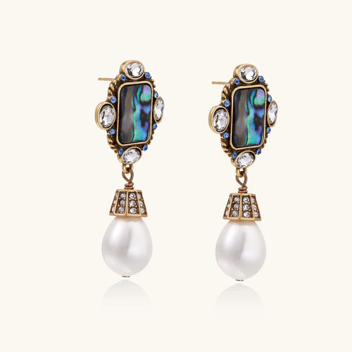 Ornate gold-plated earrings with iridescent abalone shell, crystals, blue stones, and white pearl drops on cream background.