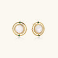 Circular gold stud earrings with iridescent mother-of-pearl center and green zirconia accents on cream background.