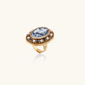 Gold-plated ring with oval blue floral cameo, pearl accents, and black enamel detailing on white background.