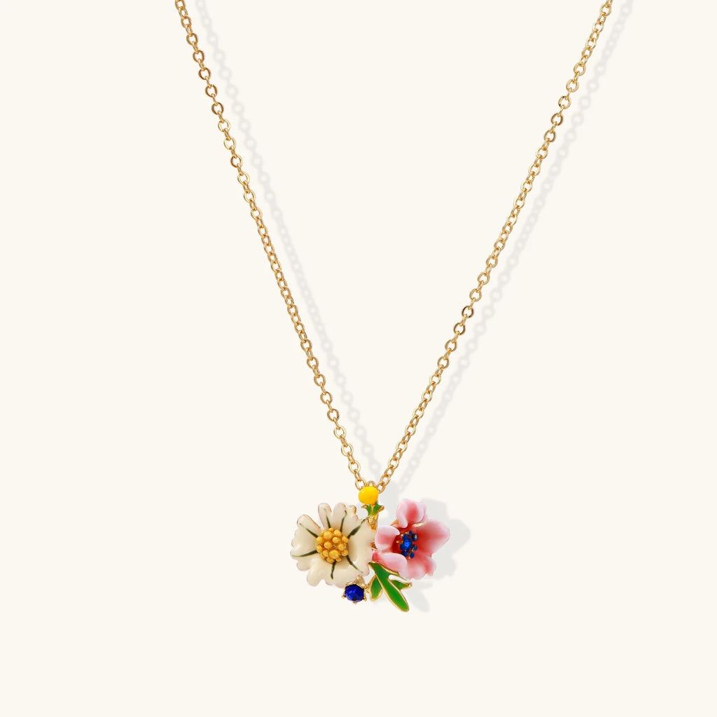 Enamel floral pendant necklace with white daisy, pink flower, yellow and blue accents on gold chain against cream background.