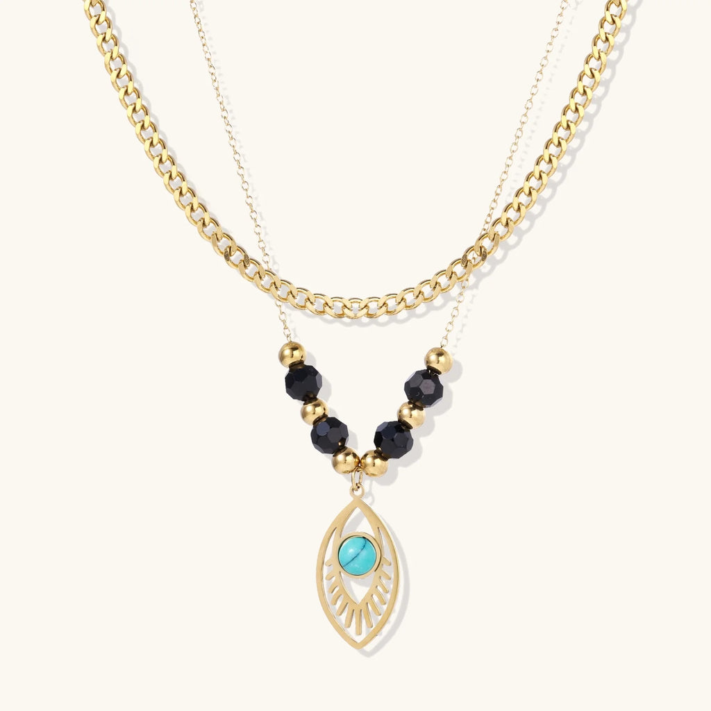 Layered gold necklace with turquoise evil eye pendant and black quartz beads on cream background
