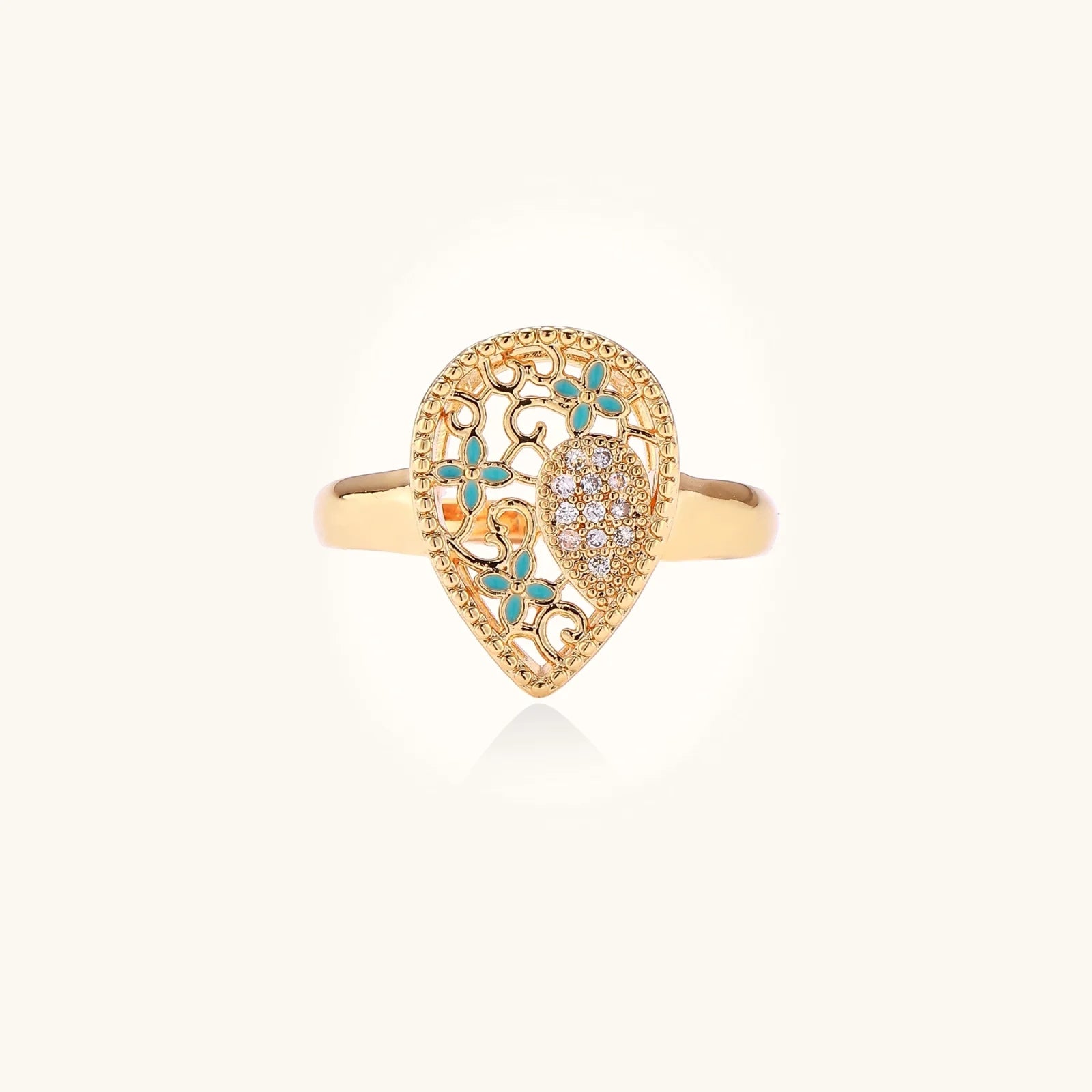 Teardrop-shaped gold-plated ring with turquoise enamel flowers and crystal pavé detail on cream background