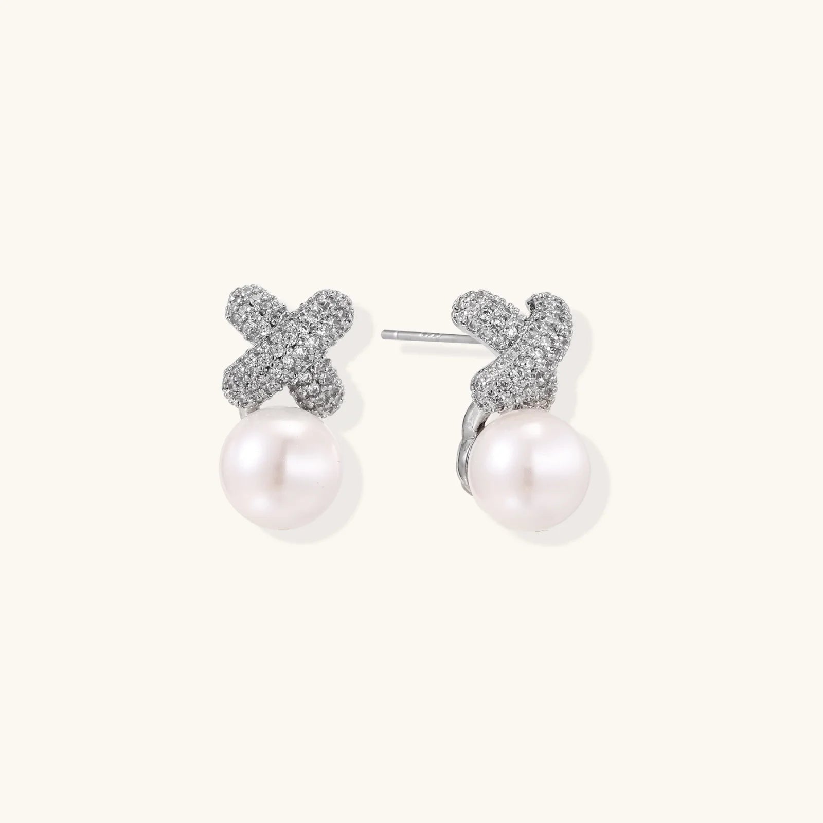 White gold plated studs featuring pavé X-shaped tops with freshwater pearl drops on cream background.