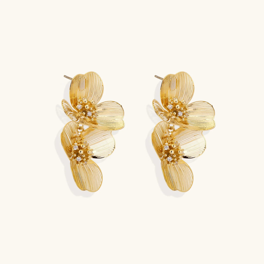 Pair of gold-plated double flower earrings with textured petals and crystal centers on cream background.