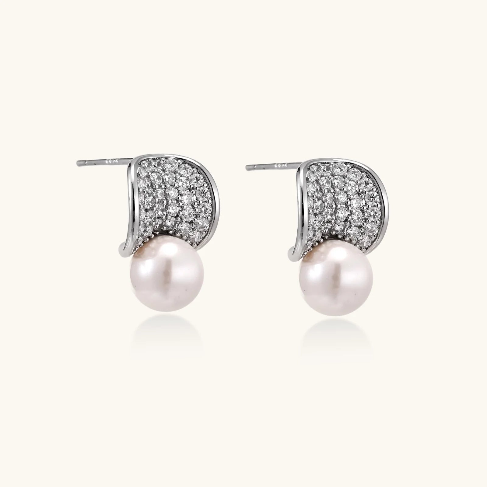 Curved pavé diamond studs in white gold-plated brass cradle lustrous freshwater pearls against cream background