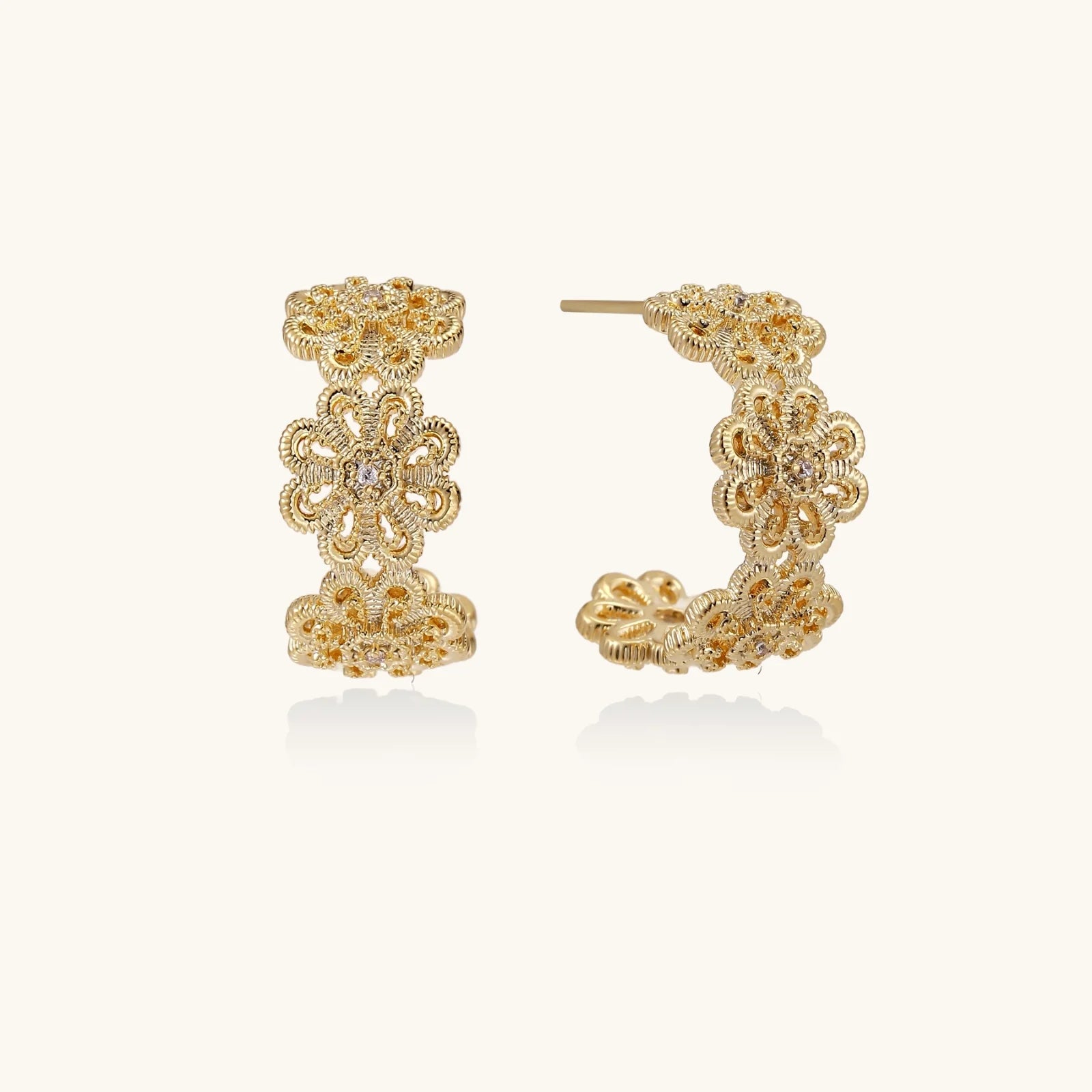 Gold hoop earrings with intricate three-dimensional floral filigree pattern in 14K gold plated brass on cream background