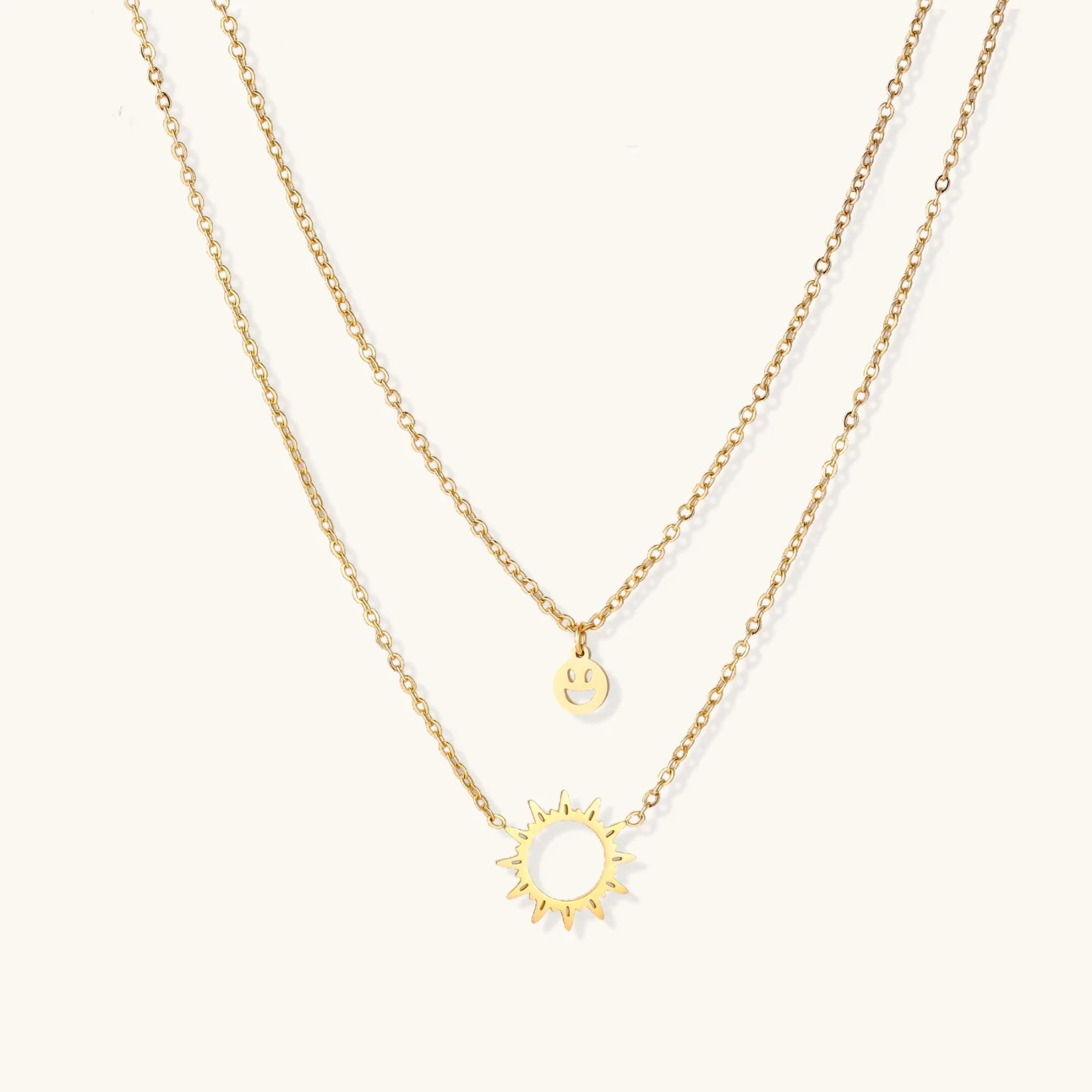 Gold layered necklace set with sunburst and smiley face pendants on delicate chains against white background.