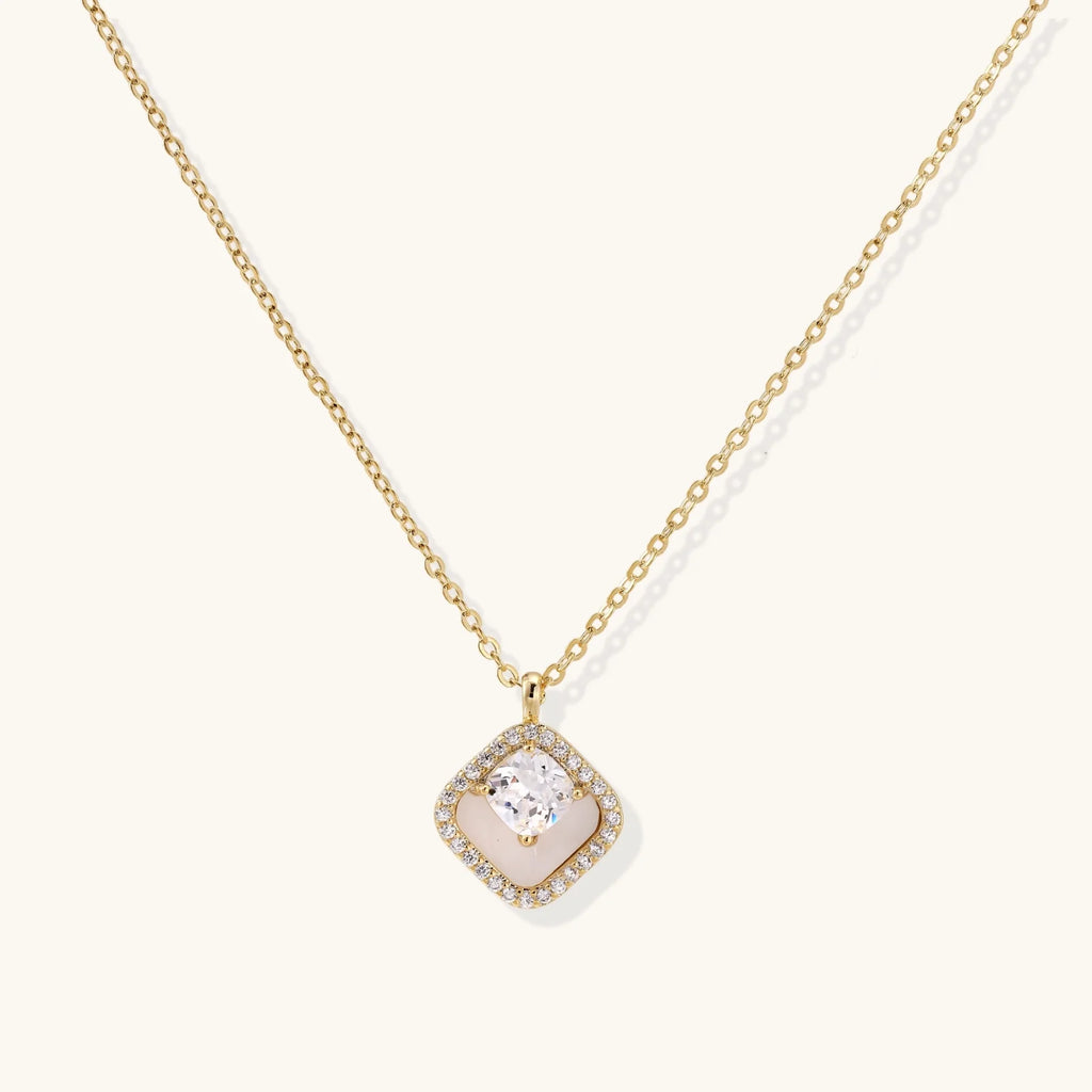 Gold quatrefoil pendant with crystal center on iridescent mother-of-pearl base, adjustable gold chain on cream background