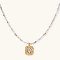 Ornate gold-plated pendant necklace with multicolored gemstone beads in purple, pink and clear tones on white background